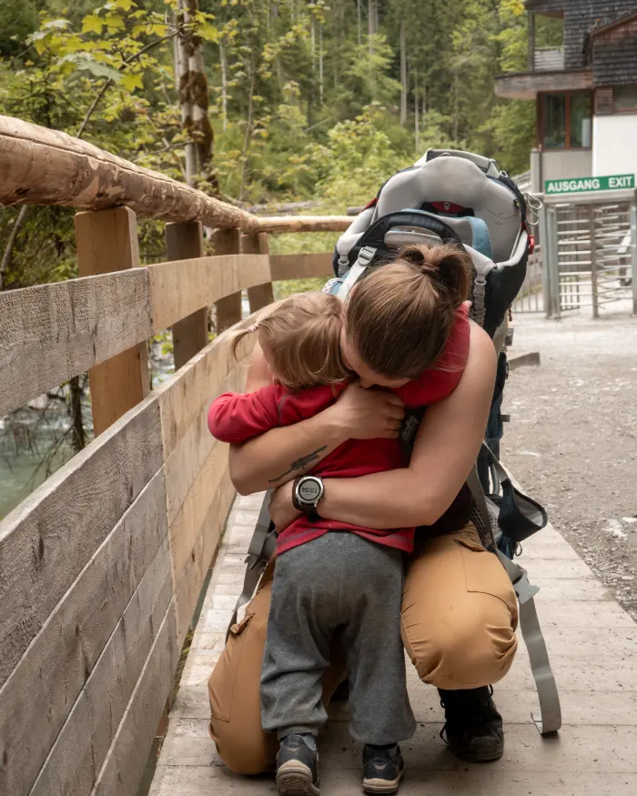 A mother crouching on a wooden bridge, hugging her toddler
